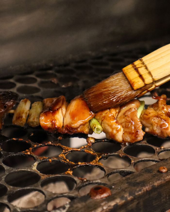 Espetos de yakitori na grelha sendo pincelados com molho