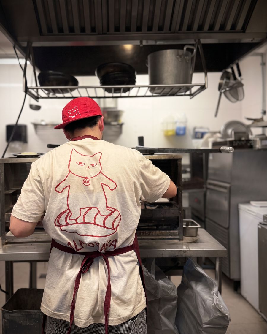 Cozinheiro de costas na cozinha do Kadoya, com o Neko estampado na camiseta